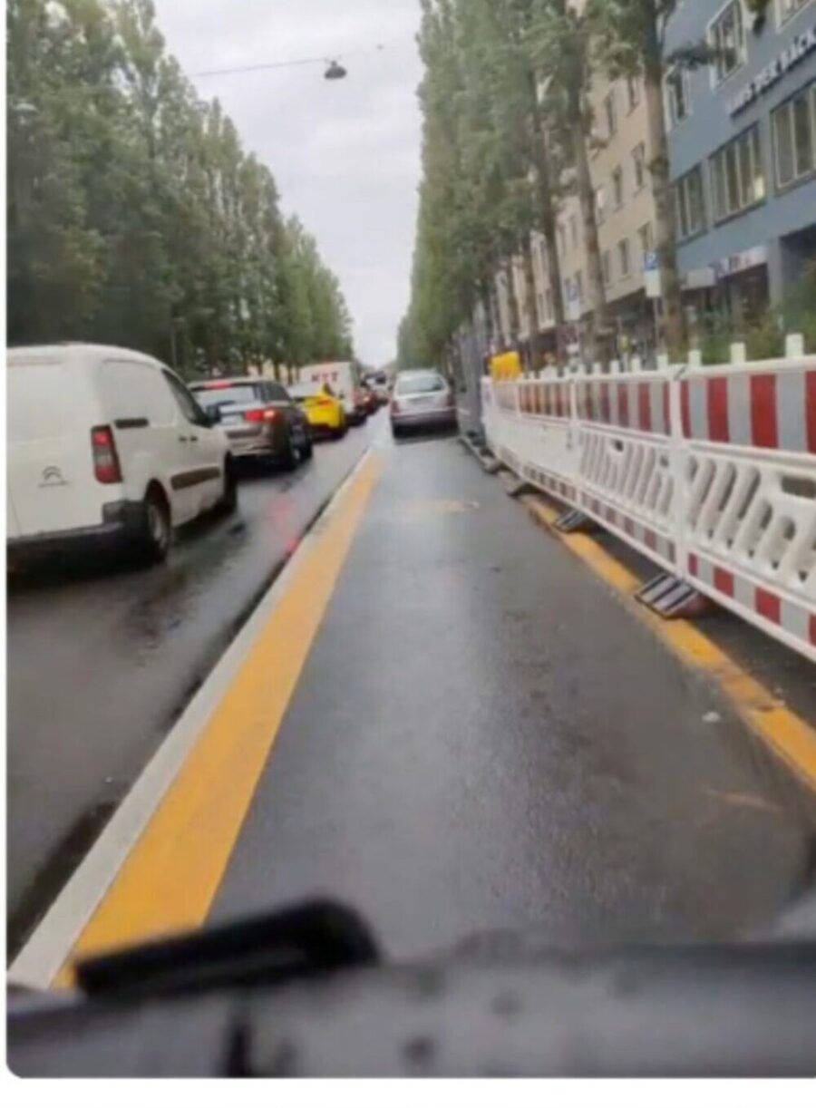 Rider's view: the protected lane runs beside parked vans with red-and-white barriers along its length in wet conditions.