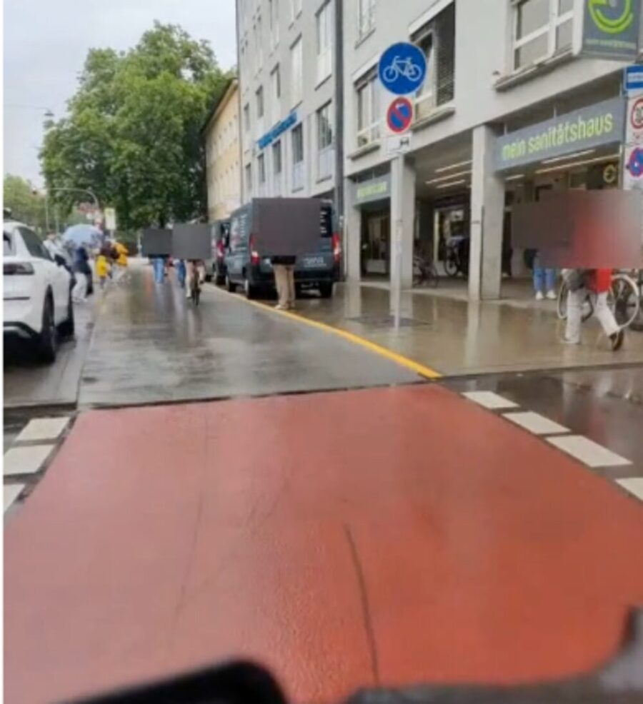 Rider's view: a red-surfaced cycle crossing at a side street with pedestrians and vehicles alongside.