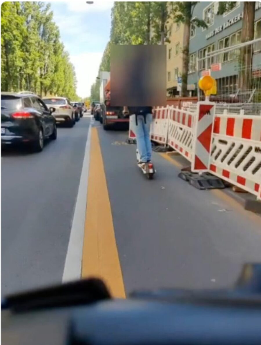 Rider's view: construction barriers to the right of the lane, an e-scooter rider ahead within the carriageway.